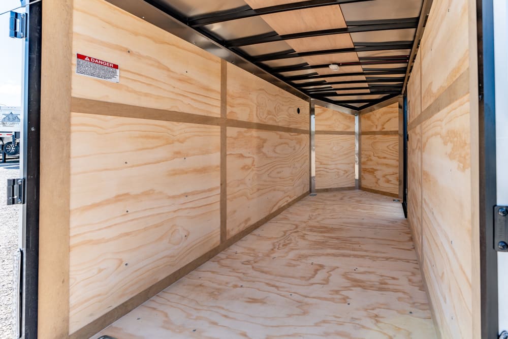 Empty cargo trailer interior with plywood walls and floor, metal framing, viewed from open rear doors.