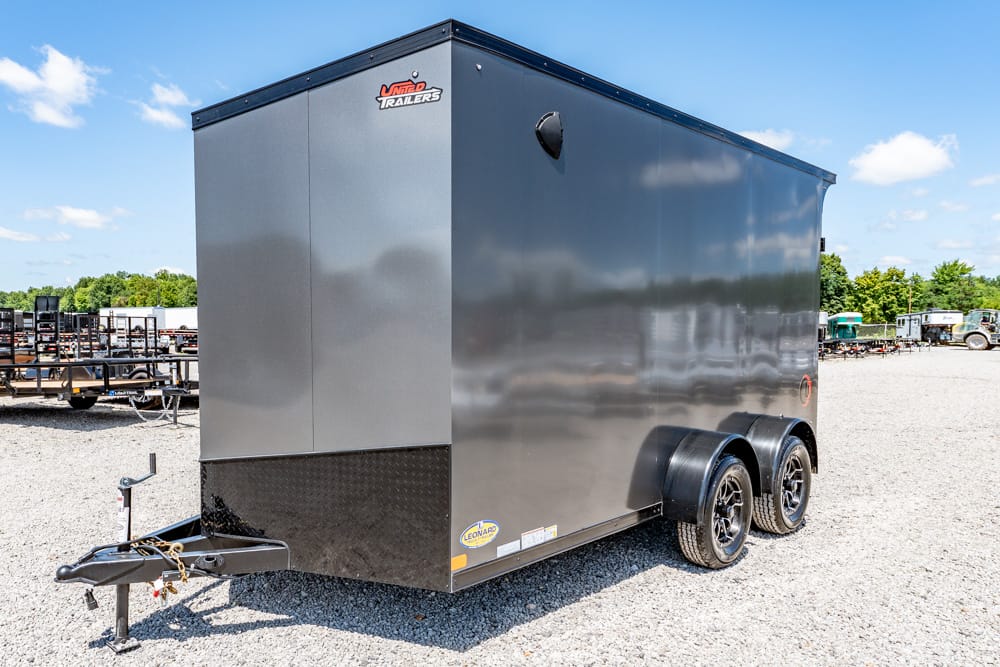 Black enclosed cargo trailer with tandem axles on a gravel lot, hitch and jack at the front, showroom-style outdoors.