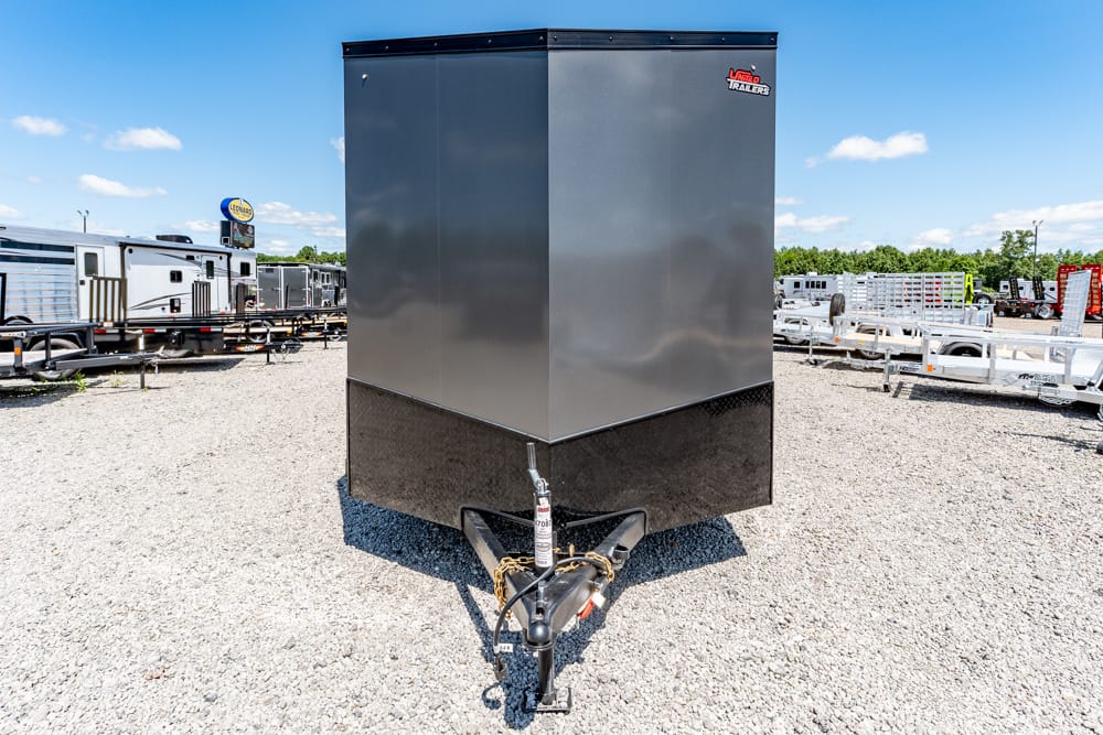 Front view of a large gray enclosed trailer on a gravel lot, with other trailers in the background.
