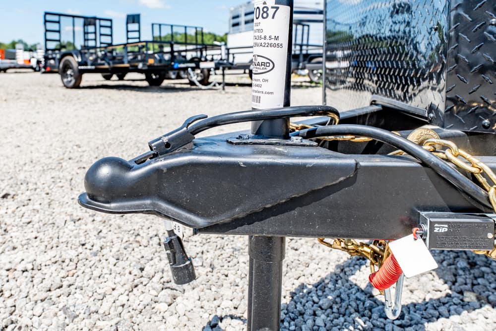 Close-up of a trailer hitch on a black frame with a chain and lock, parked on a gravel lot.