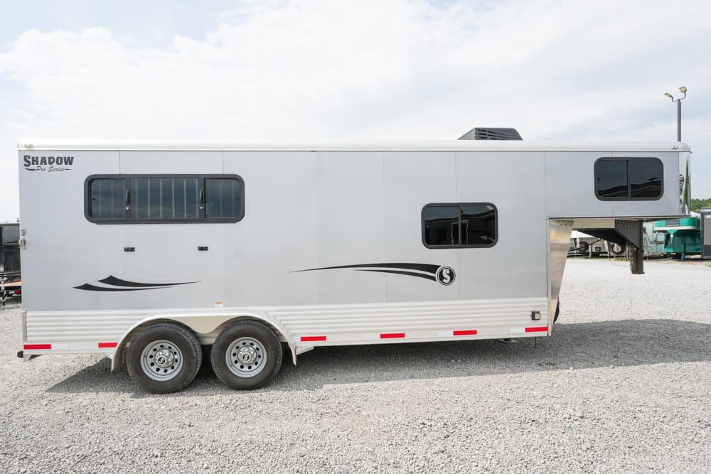 Silver gooseneck horse trailer with two axles, windows, and decorative black swoosh graphics on a gravel lot