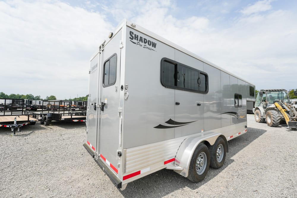 Silver Shadow Pro Series enclosed trailer with tandem wheels in a gravel lot, showing side decals and windows.