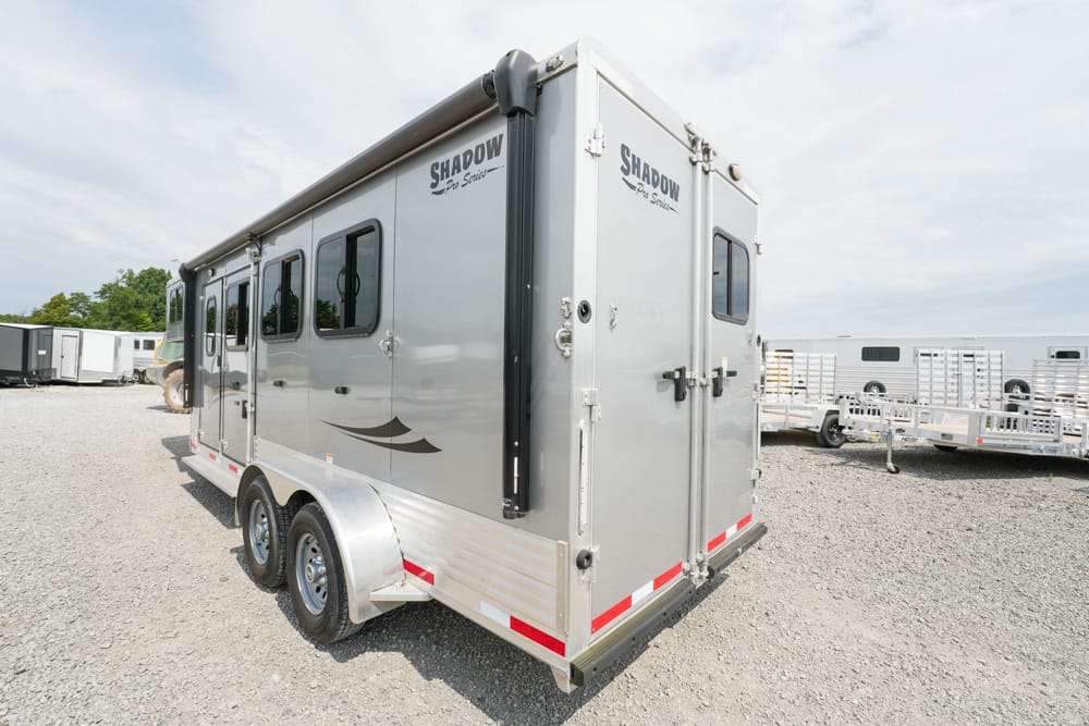 Silver Shadow Pro Series horse trailer with two axles, side windows, and rear double doors on a gravel lot nearby other trailers.