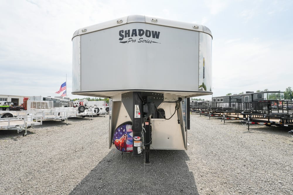 Front view of a Shadow Pro Series gooseneck trailer in a gravel lot among other trailers.