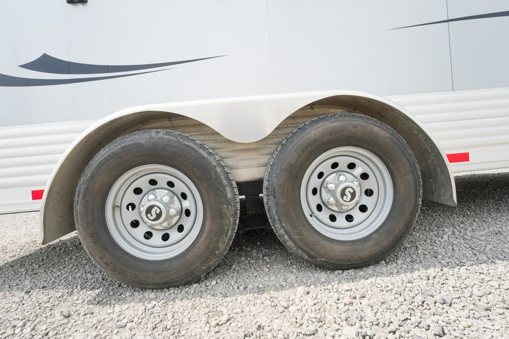 Close-up of twin trailer wheels under a curved fender on a gravel surface.