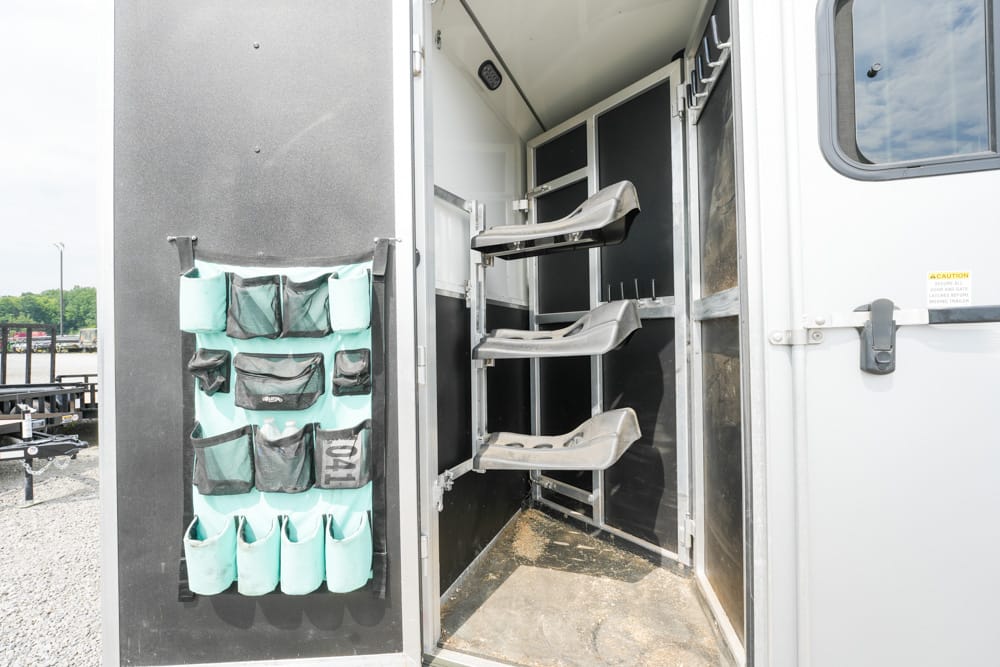 Interior of a horse trailer with three saddle racks and a hanging pocket organizer on the door for gear storage.