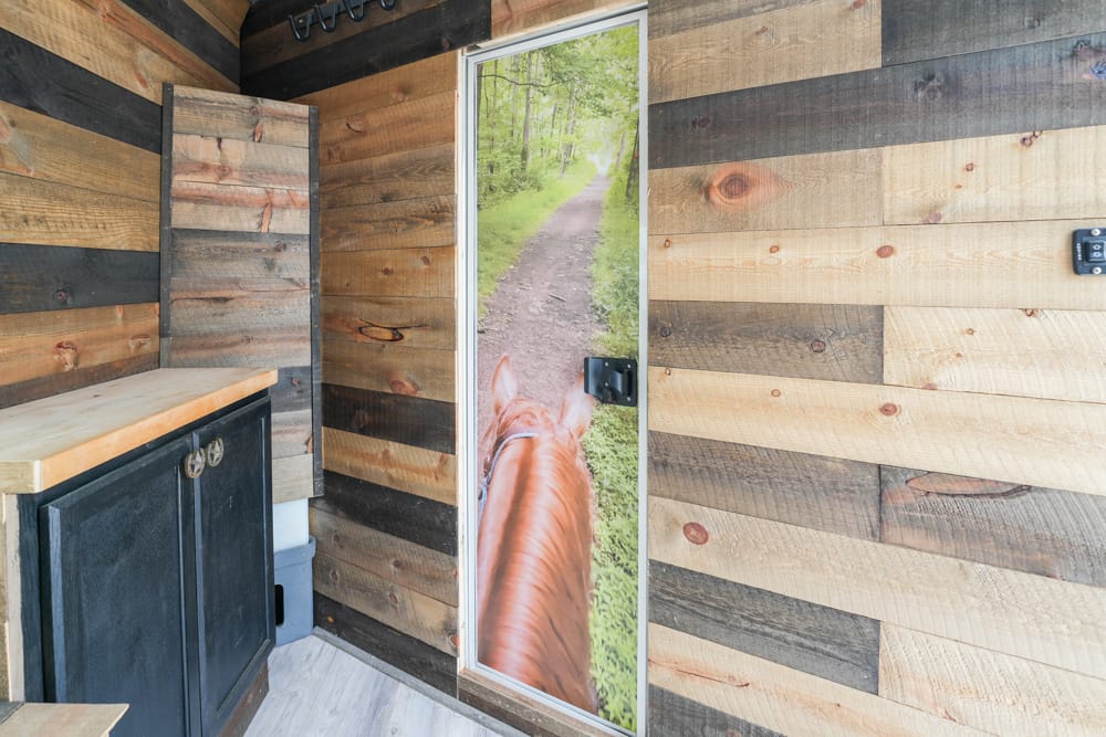 Door featuring a horse's head photo, showing a forest trail; opens to the outdoors from a wood-paneled room.