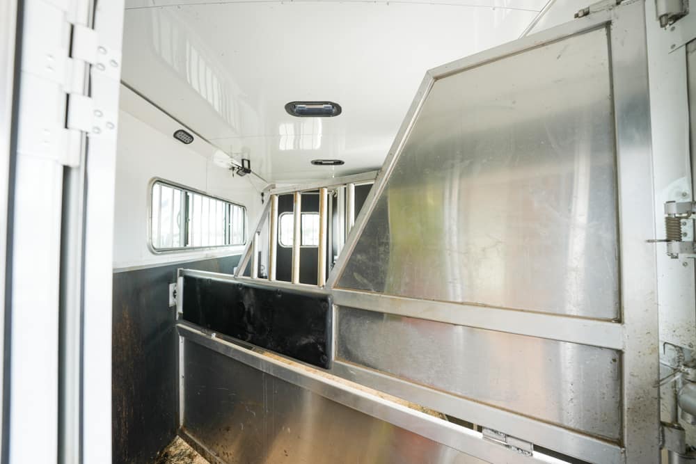 Interior of a metal livestock trailer with partition panels and side windows along the wall.