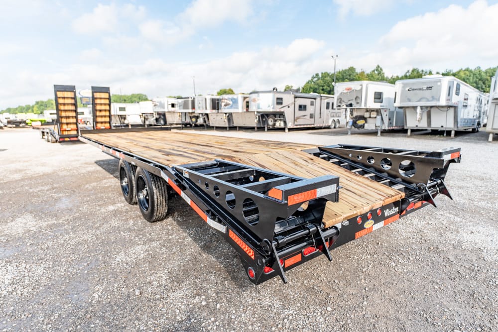Black heavy‑duty flatbed trailer with a wooden deck and dual axles, parked in a lot of RVs and trailers in the background.