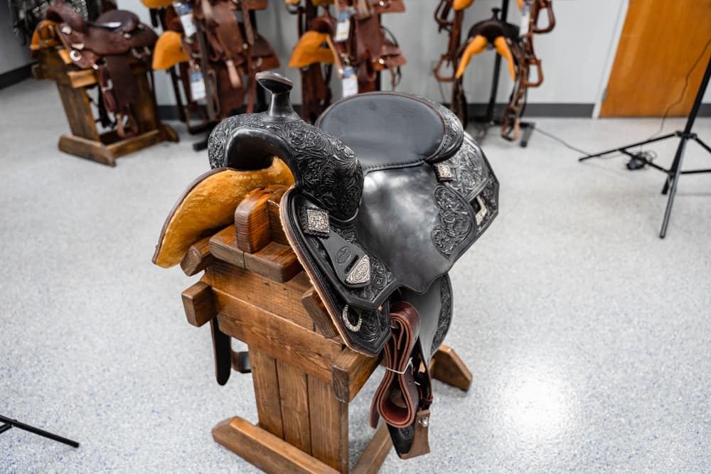 Leather Western saddle with decorative tooling on a wooden saddle stand in a tack room, other saddles in the background
