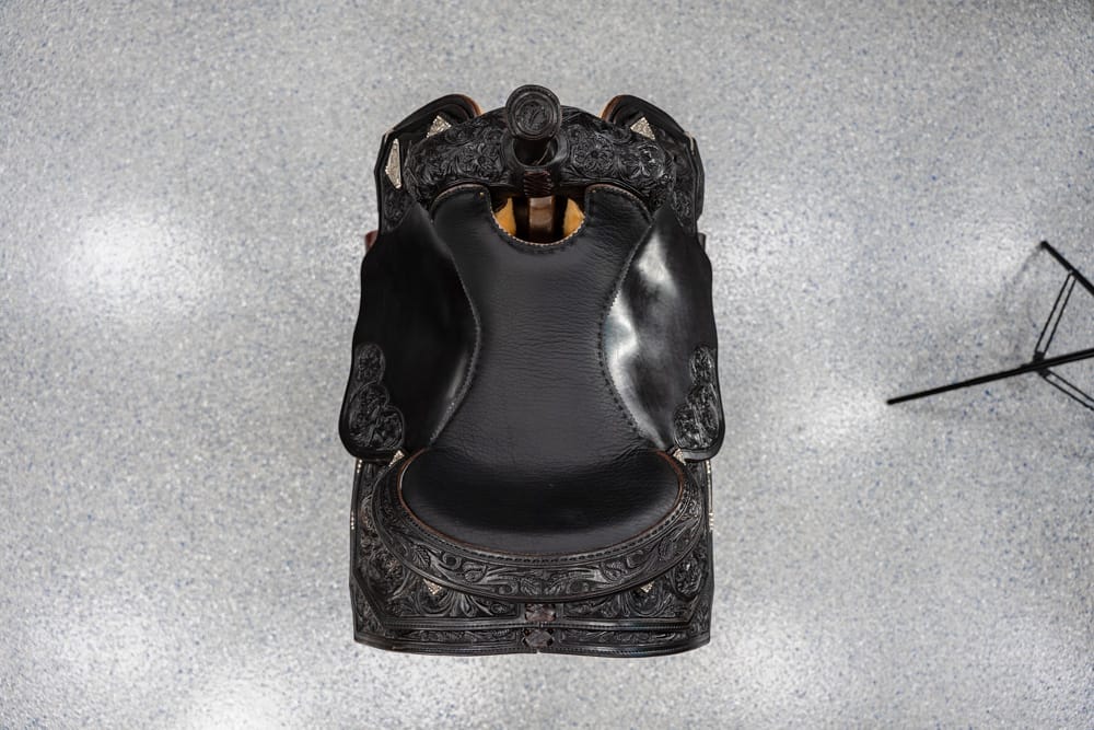 Ornate black Western saddle viewed from above on a speckled floor.