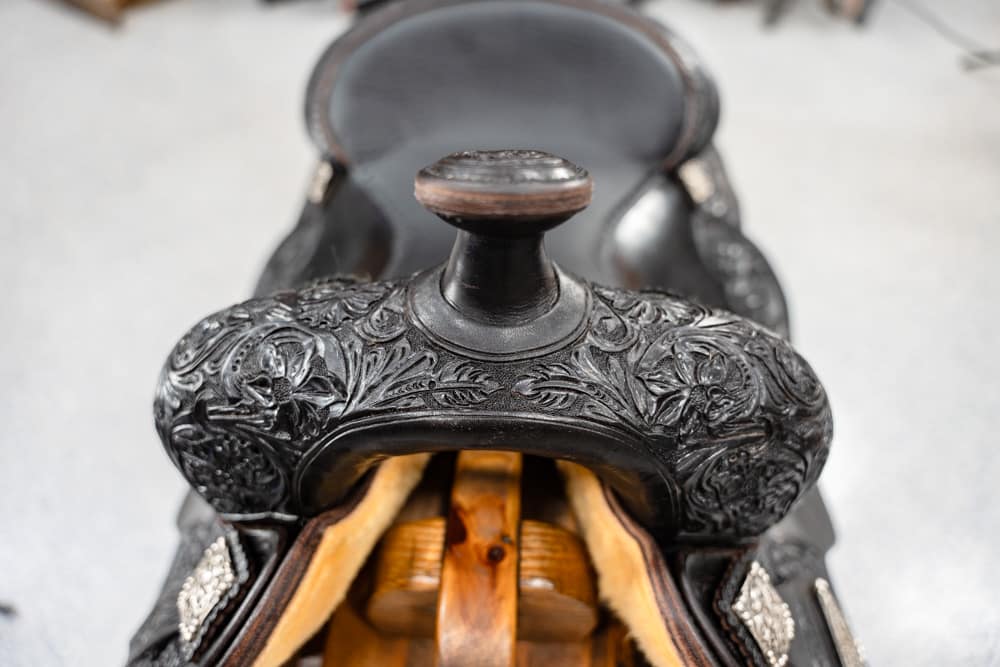 Close-up of a carved leather saddle with intricate floral tooling and wooden components visible beneath the seat.