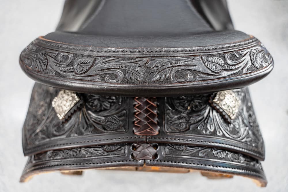 Close-up of a black tooled leather Western saddle with floral patterns and stitched detailing.