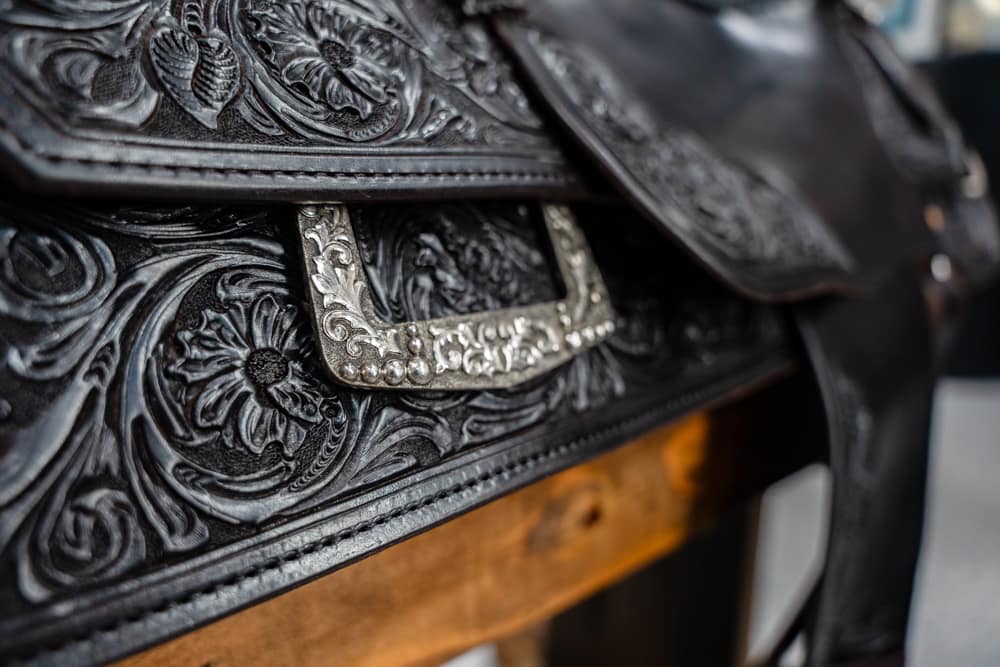 Close-up of black tooled leather saddlebag with intricate floral patterns and a silver embellished buckle.