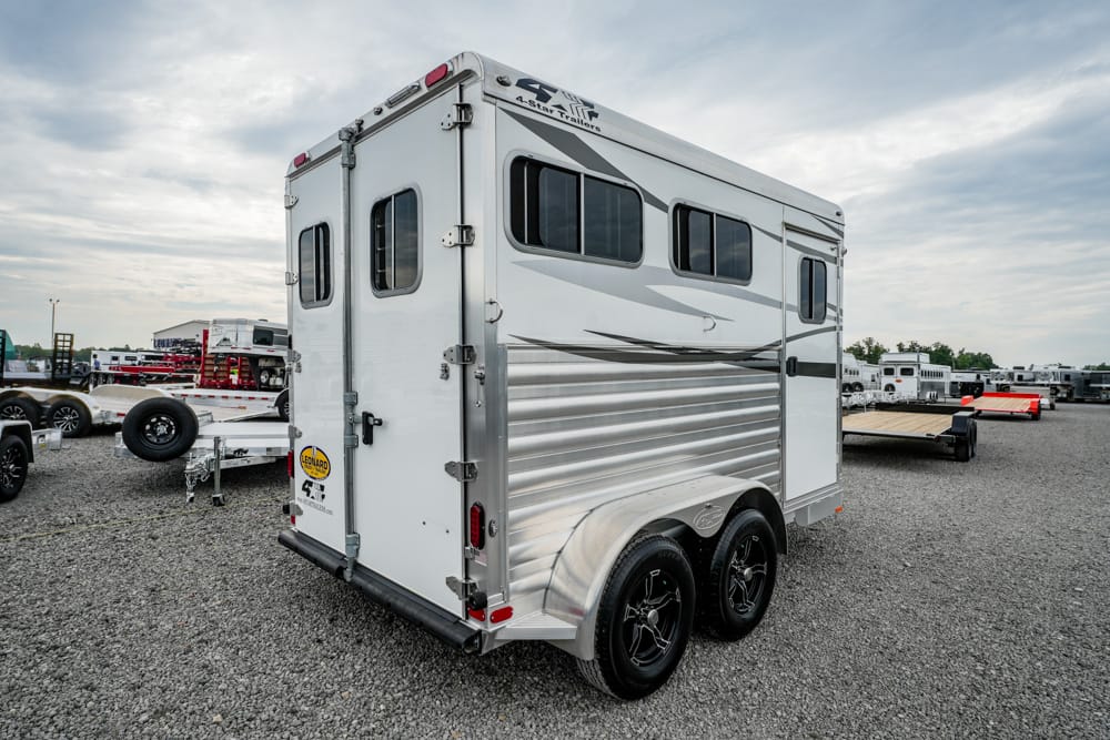 White tandem-axle horse trailer with small side windows, parked on a gravel lot.