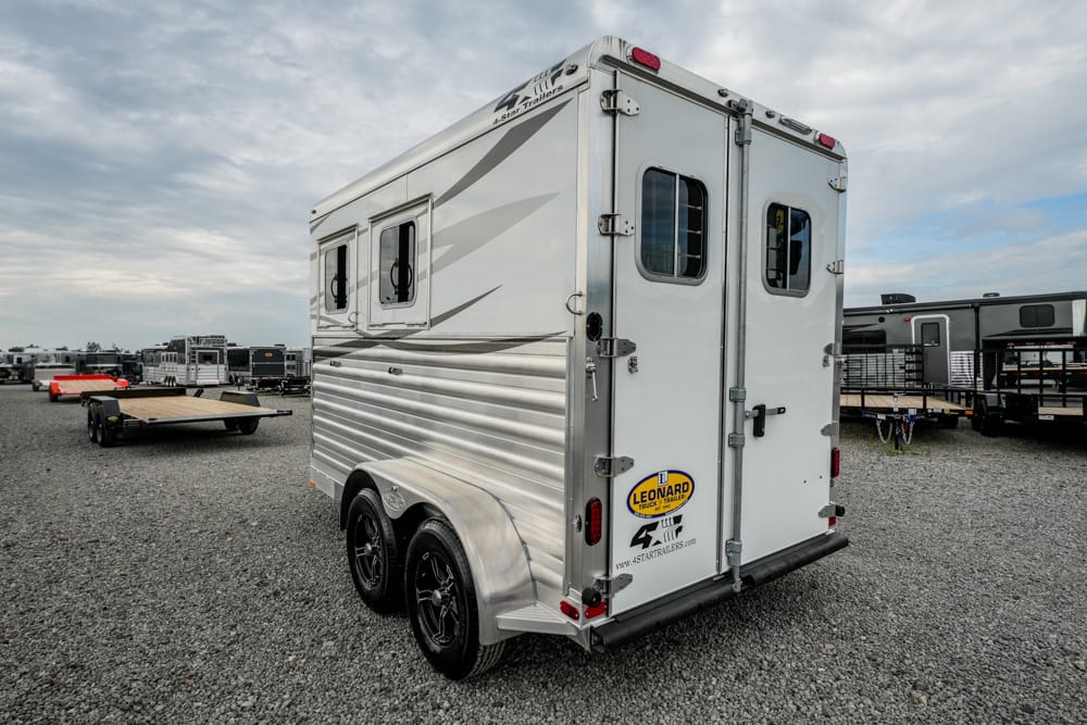 Rear view of a two-axle silver aluminum horse trailer with rear double doors and small windows on a gravel lot; Leonard trailer logo visible on the back.