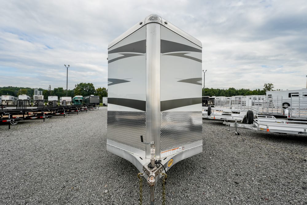 Front view of a tall, silver enclosed cargo trailer with diamond-plate lower edge in a gravel trailer lot.