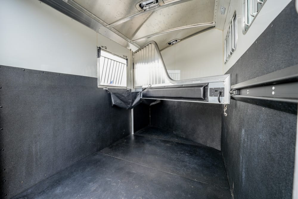 Interior of an empty horse trailer with a padded divider and dark rubber flooring