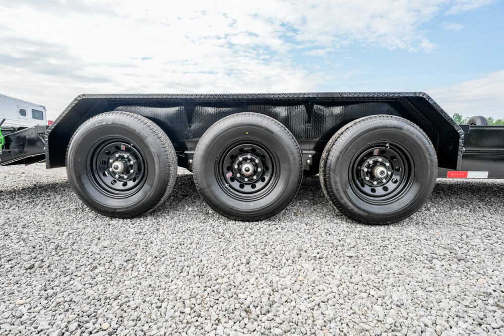 Side view of a black heavy-duty trailer with three axles and large tires on a gravel surface.
