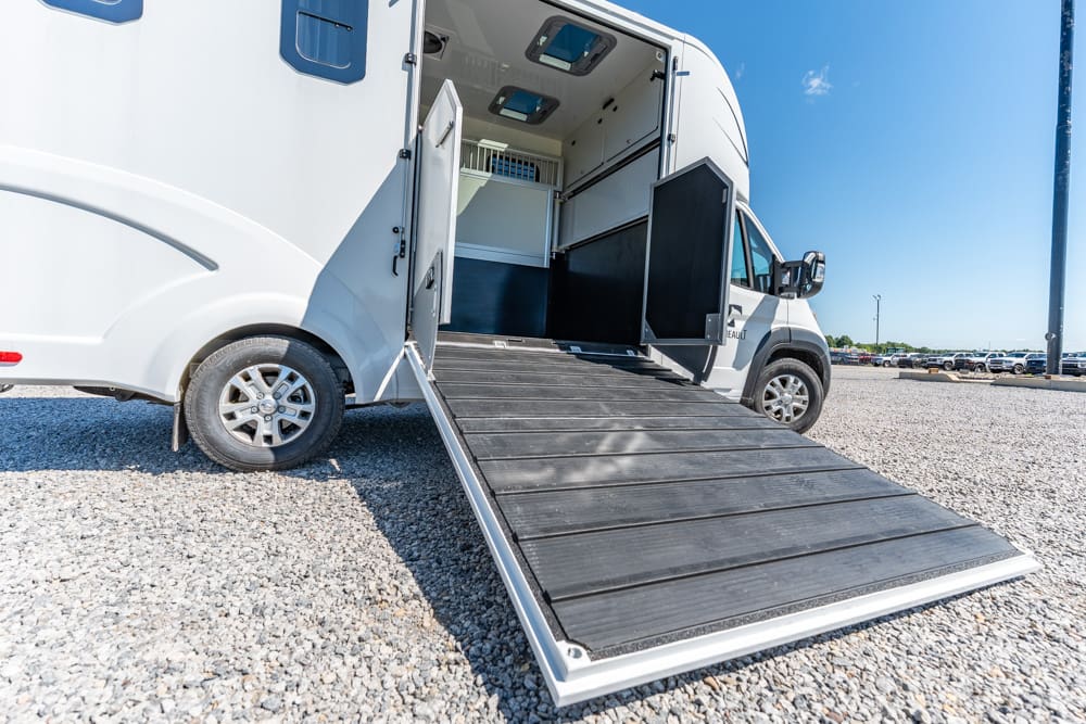 White recreational vehicle with a lowered wheelchair ramp extended to the ground on a gravel parking lot.