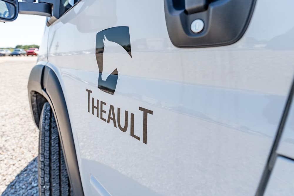 White van door displaying Theault logo and brand name, with a stylized shield and horse head emblem on the side.