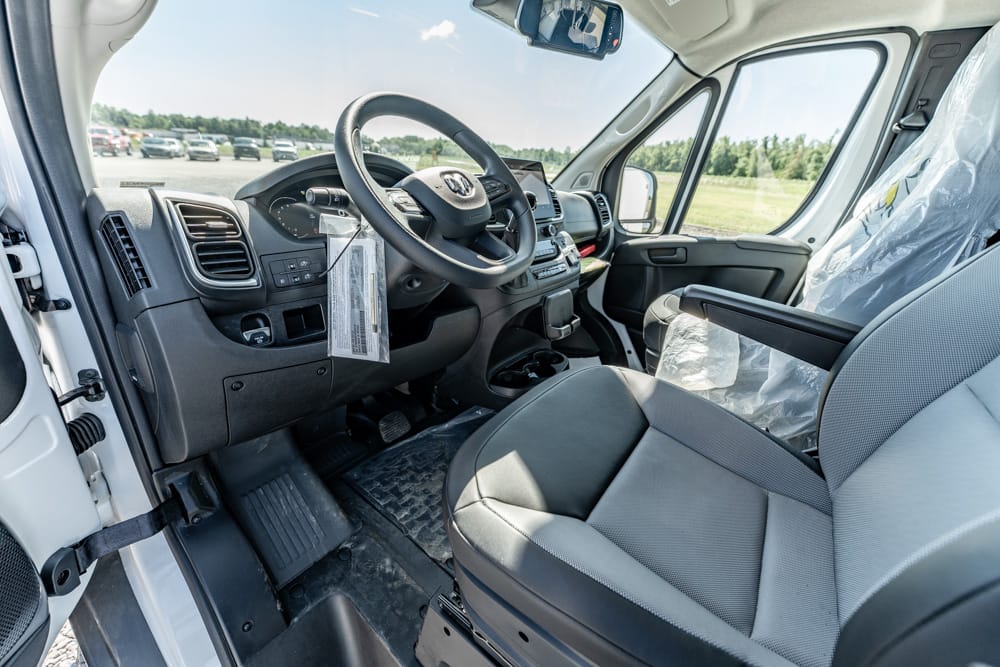 Driver's seat and dashboard of a white van, with steering wheel and controls visible in a parking lot.