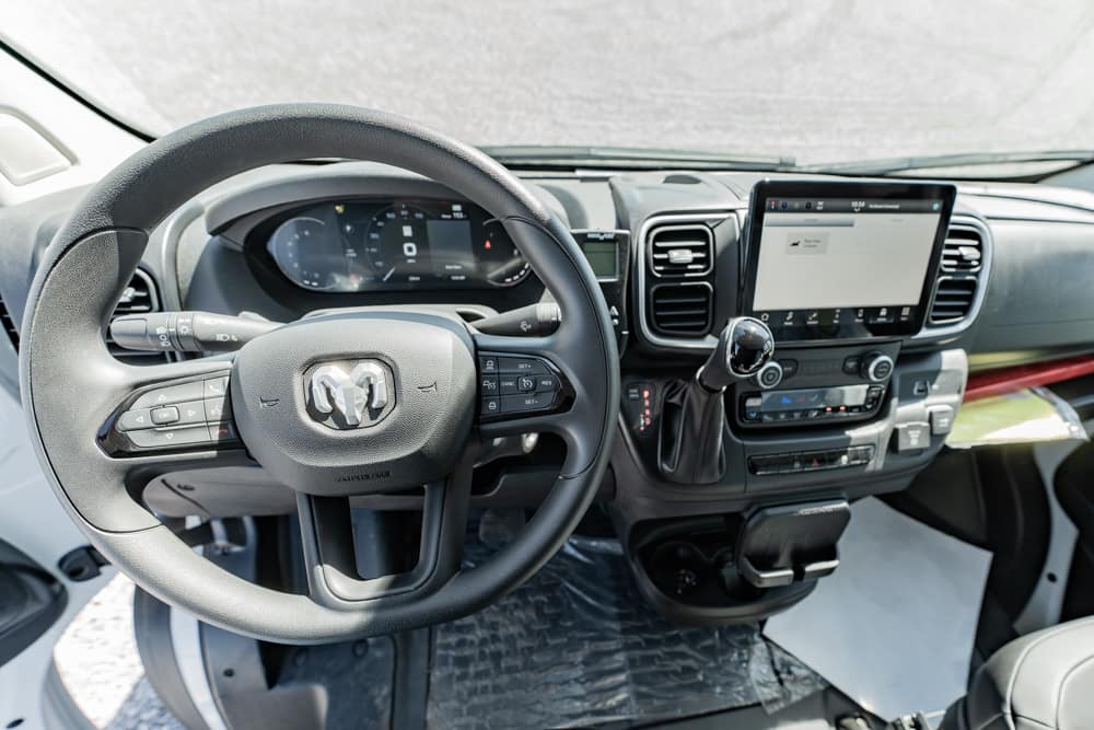 Dashboard view of a modern van interior with a steering wheel, digital gauge cluster, and a large central touchscreen display behind the steering wheel.