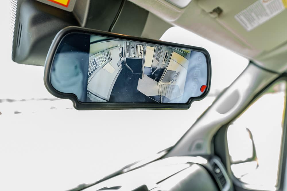 Rearview mirror reflecting the inside of a vehicle with seats and an aisle visible behind the driver