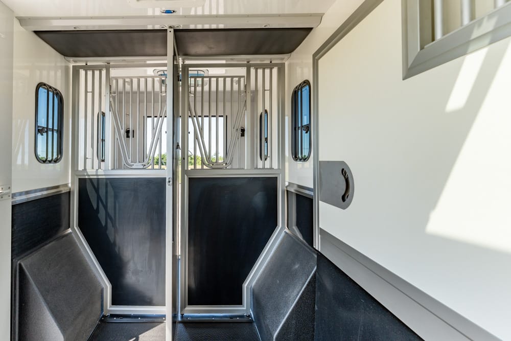 Interior of a white horse trailer with two stalls, metal divider bars, and black rubber lower walls, ready for horses