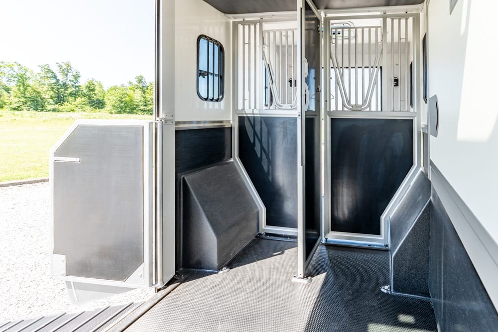 Interior of a horse trailer showing two stalls with metal dividers and a non-slip rubber floor