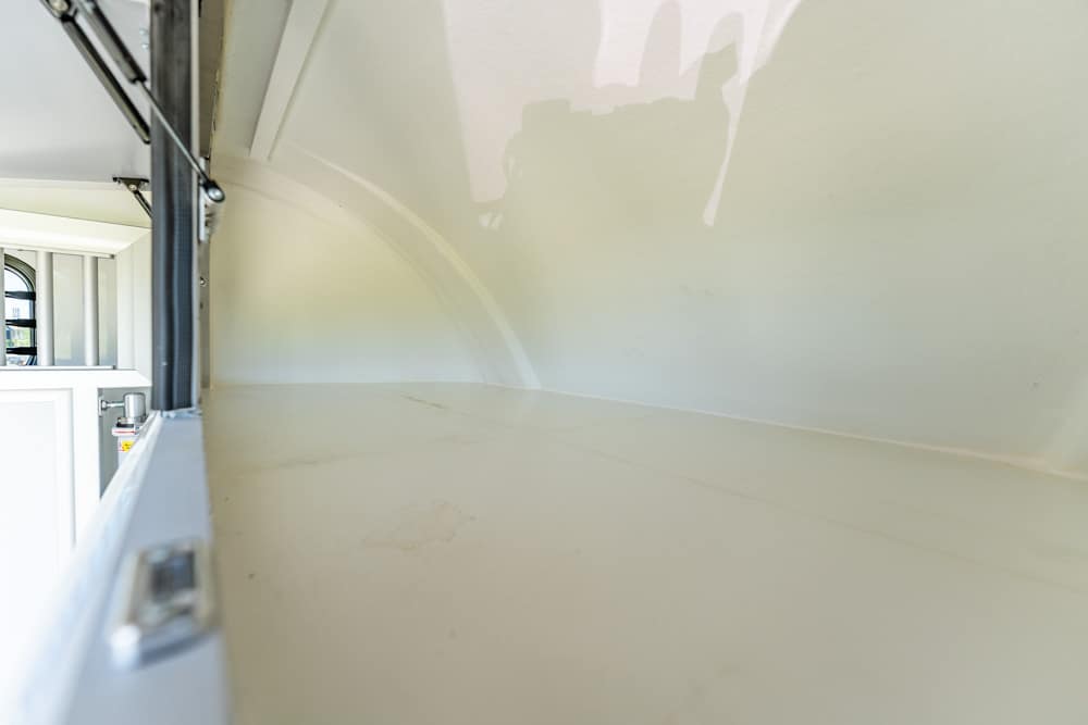 Interior of a light-colored cargo trailer with a curved wall and a white cabinet along the left side, empty and clean.