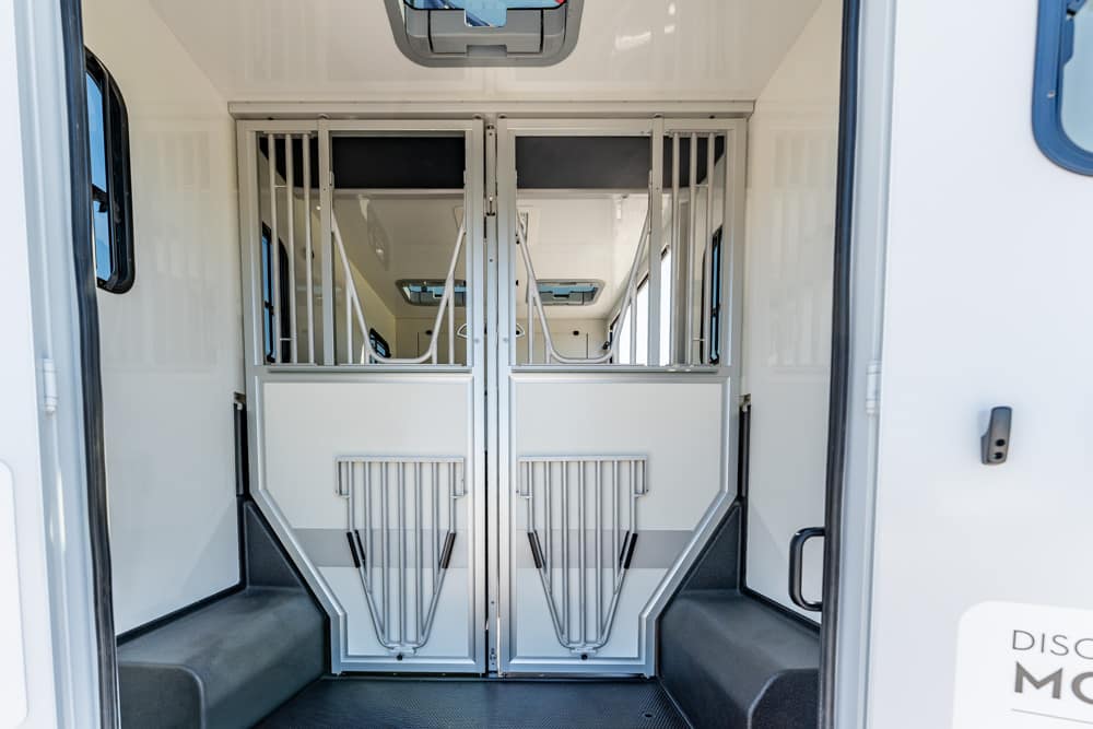 Interior of a white horse trailer with two partitioned stalls and metal gates, ready for horses.