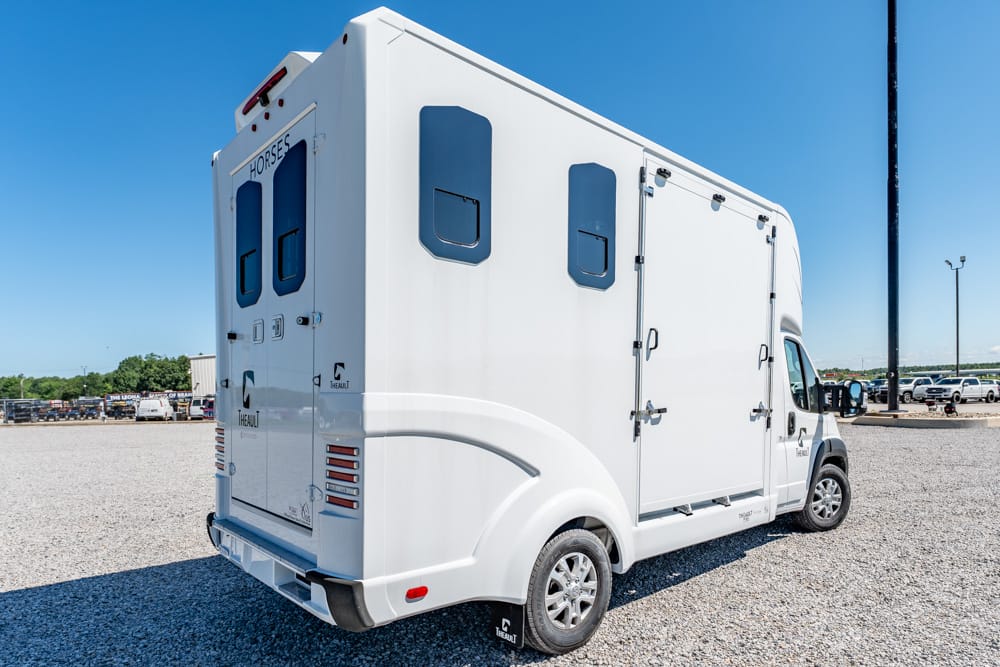 White horse transport truck with rear double doors and side compartments parked on a gravel lot under a clear blue sky.