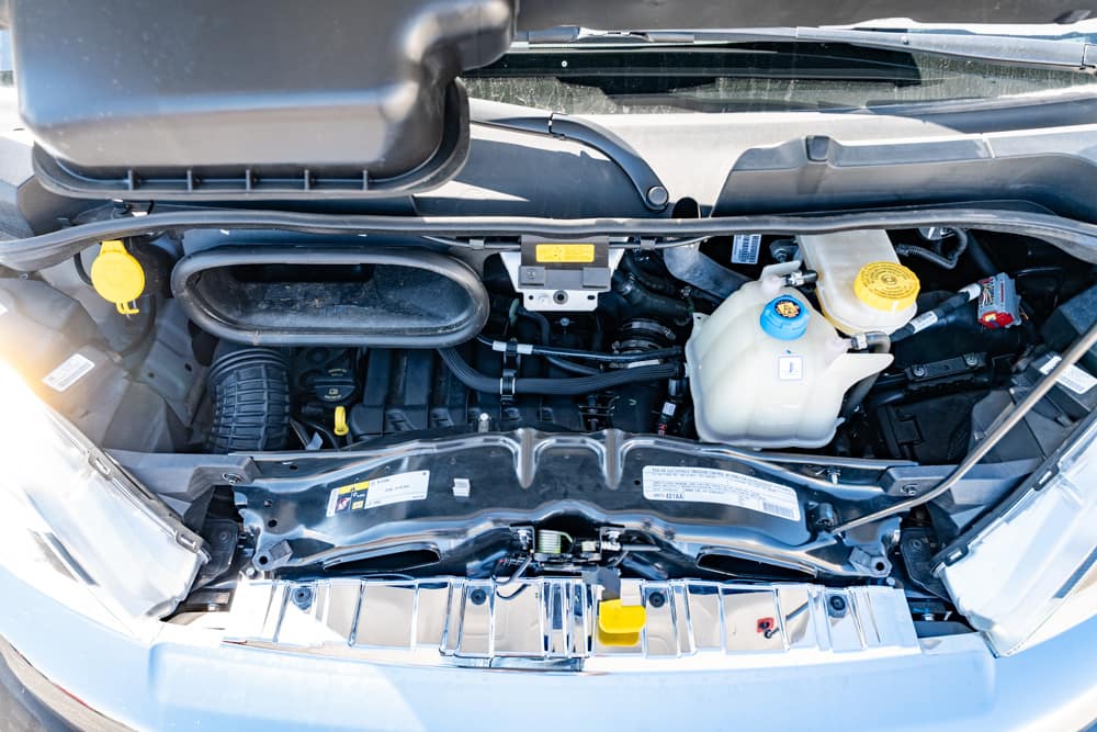 Front view of a car engine bay with coolant reservoir, yellow dipstick, and various hoses under the open hood