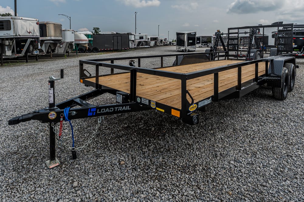 Black Load Trail flatbed trailer with wooden deck and dual axles in a trailer lot.