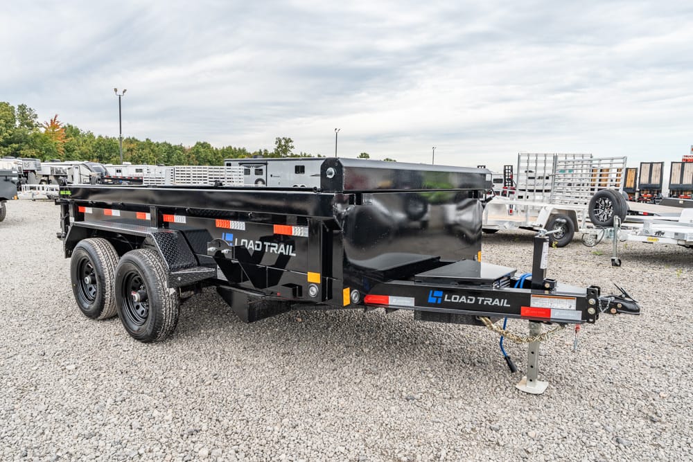 Black Load Trail dump trailer with dual rear wheels on a gravel lot, logo visible on the side, surrounded by other trailers.