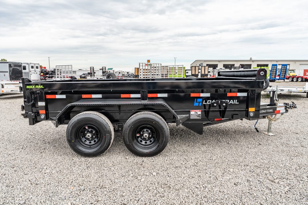 Black dual-axle dump trailer with Max Rail branding, parked on a gravel lot.