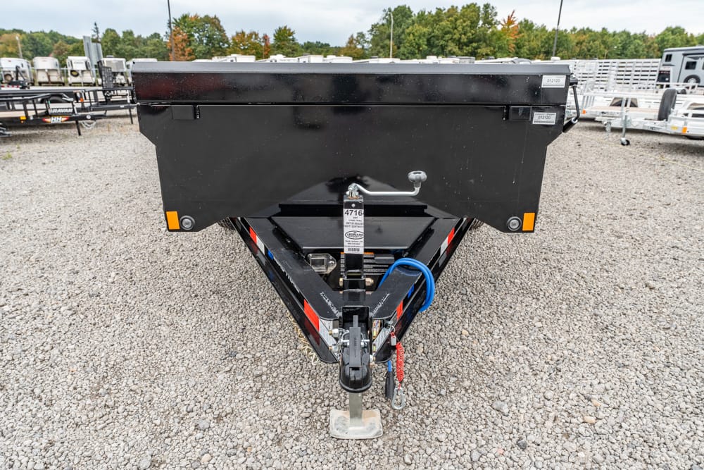 Rear view of a black dump trailer on a gravel lot, showing the hitch, jack, and safety chains with other trailers in the background.]','Rear view of a black dump trailer on a pebbled lot, featuring the hitch, stabilizer, and support leg.