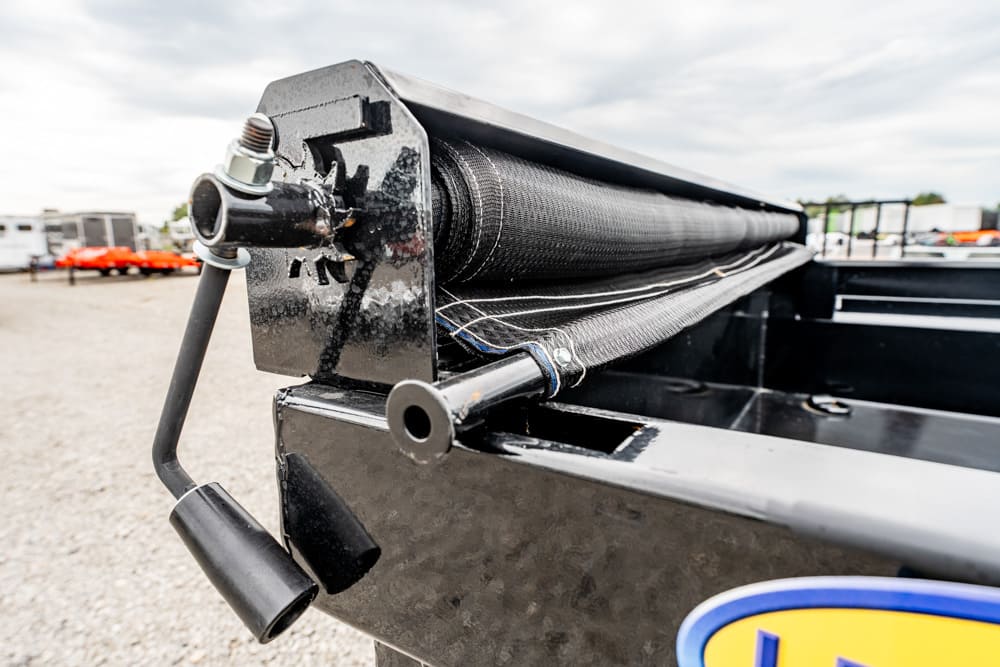 Close-up of a metal winch/roller with a crank handle on the side of a black trailer bed, used to reel in cargo.