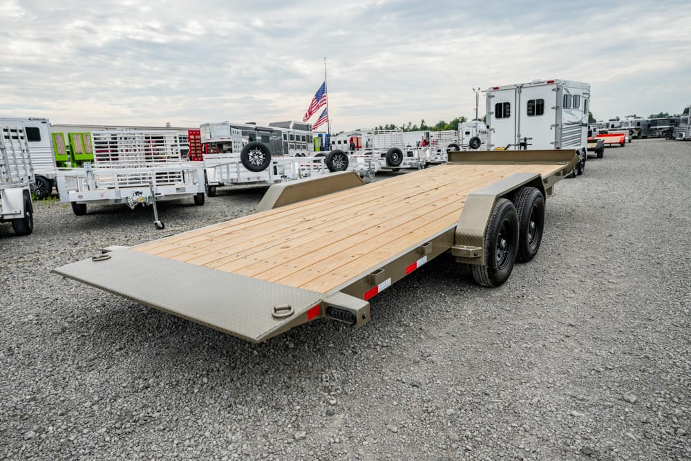 Long flatbed trailer with a wooden deck and dual rear axles in a gravel trailer lot.