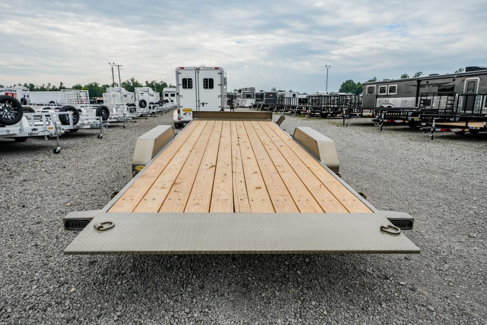 Flatbed trailer with a wooden deck in a gravel lot, surrounded by other trailers and RVs. (Informative, contextual)