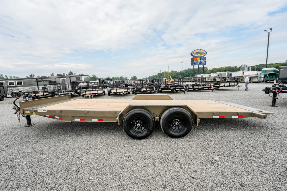 Dual-axle flatbed trailer on a gravel lot with other trailers in the background.