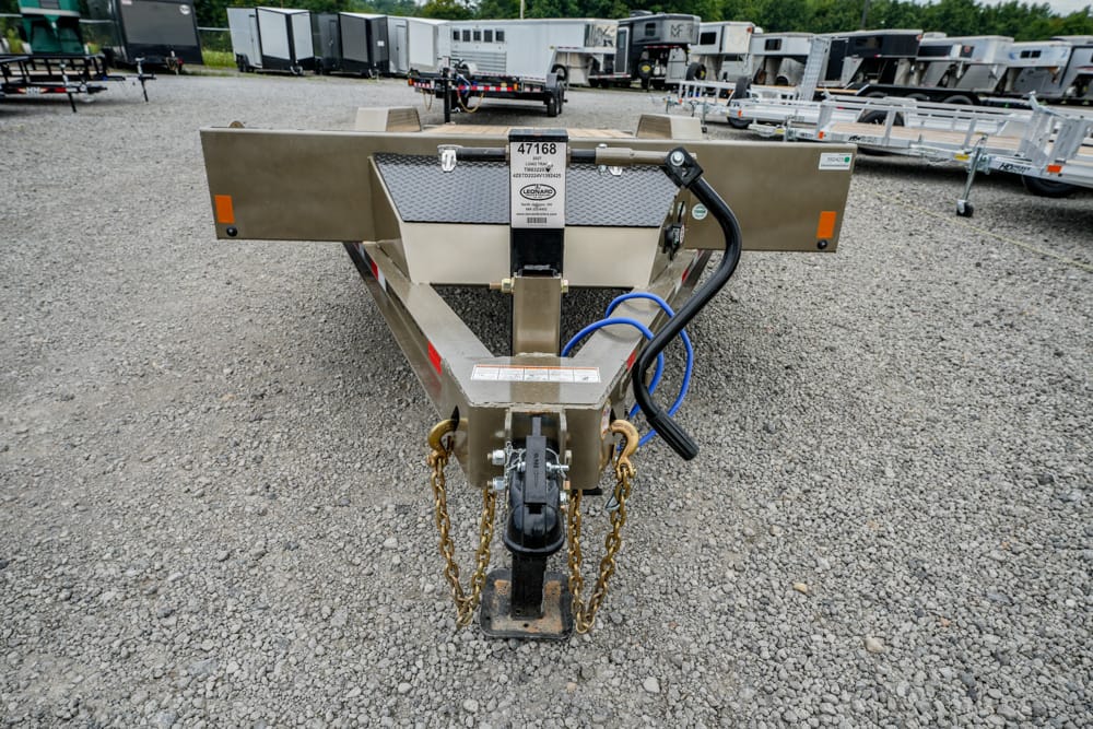 Front view of a utility trailer hitch with safety chains and blue hoses on a gravel lot among other trailers behind it.