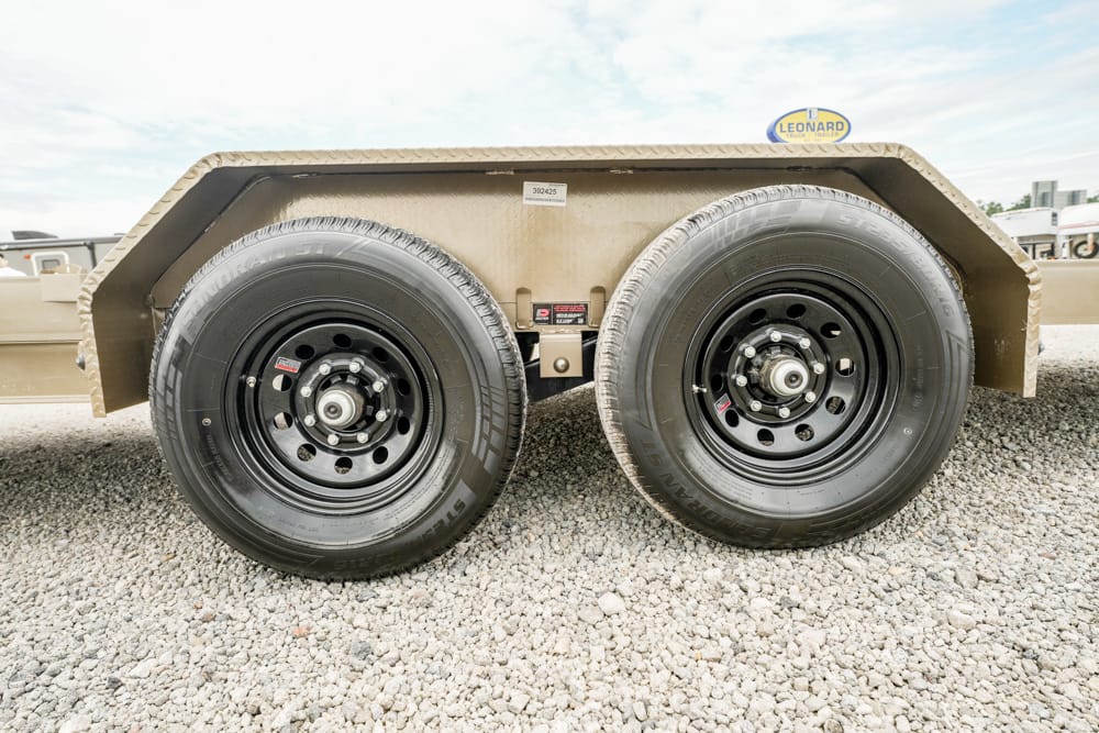 Dual-axle trailer with black steel wheels parked on gravel surface.