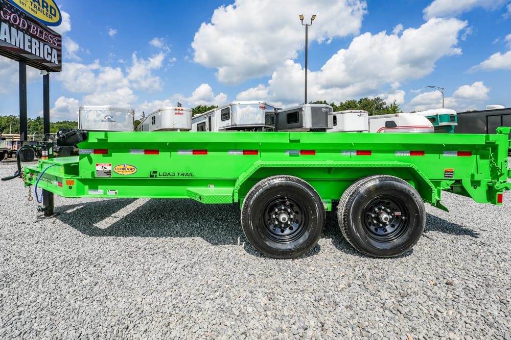 Bright green Load Trail utility trailer with dual axles parked on a gravel lot, campers visible in background.