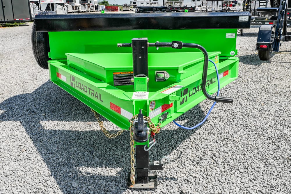 Bright green Load Trail utility trailer hitch on a gravel lot, showing its front coupling and safety chains.