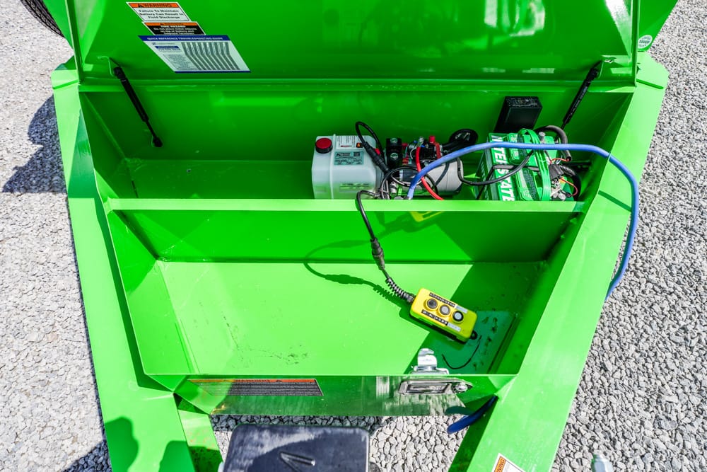 Open green machine with battery and wiring visible inside; yellow control pendant rests in lower compartment