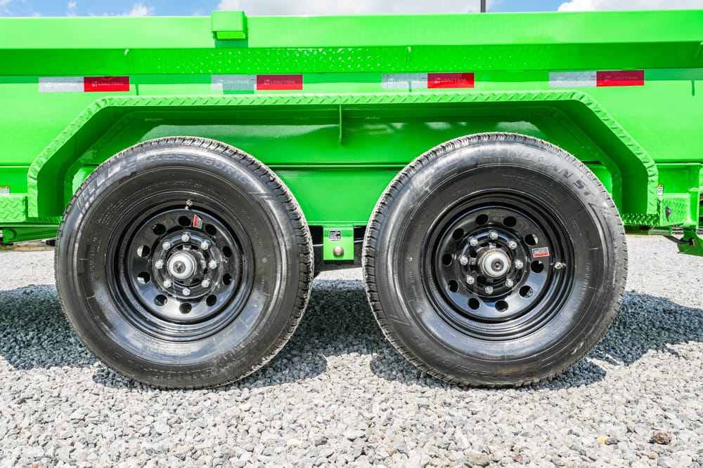 Side view of a bright green trailer with two large black wheels on a gravel surface.