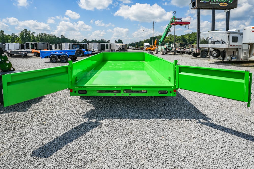 Bright green dump trailer with side gates fully opened in a truck-trailer yard, ready for loading on gravel surface.
