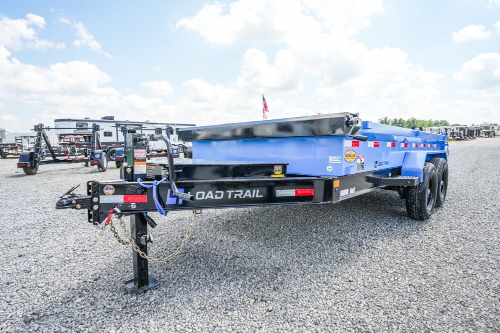 Blue Load Trail dump trailer on a gravel lot, view of hitch, chains, and dual axles visible.